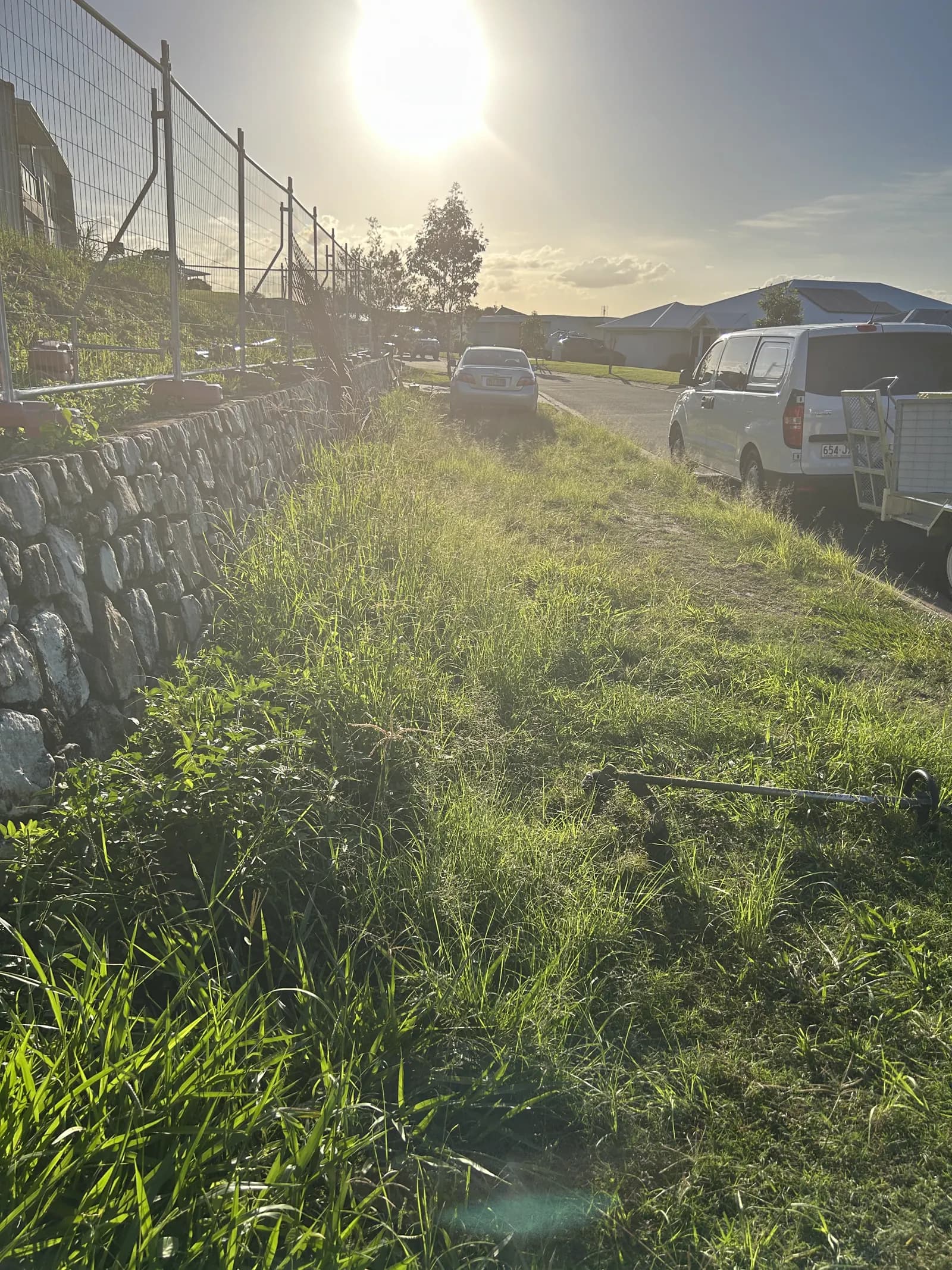 Lawn behind a rock retaining wall, tall and untidy before Lucky Duck Mowing