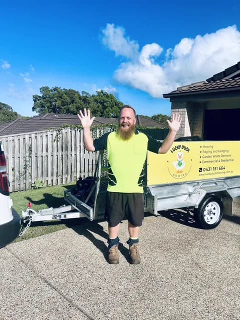 Rowan from Lucky Duck Mowing in his hi-vis with his branded trailer at home in Caloundra