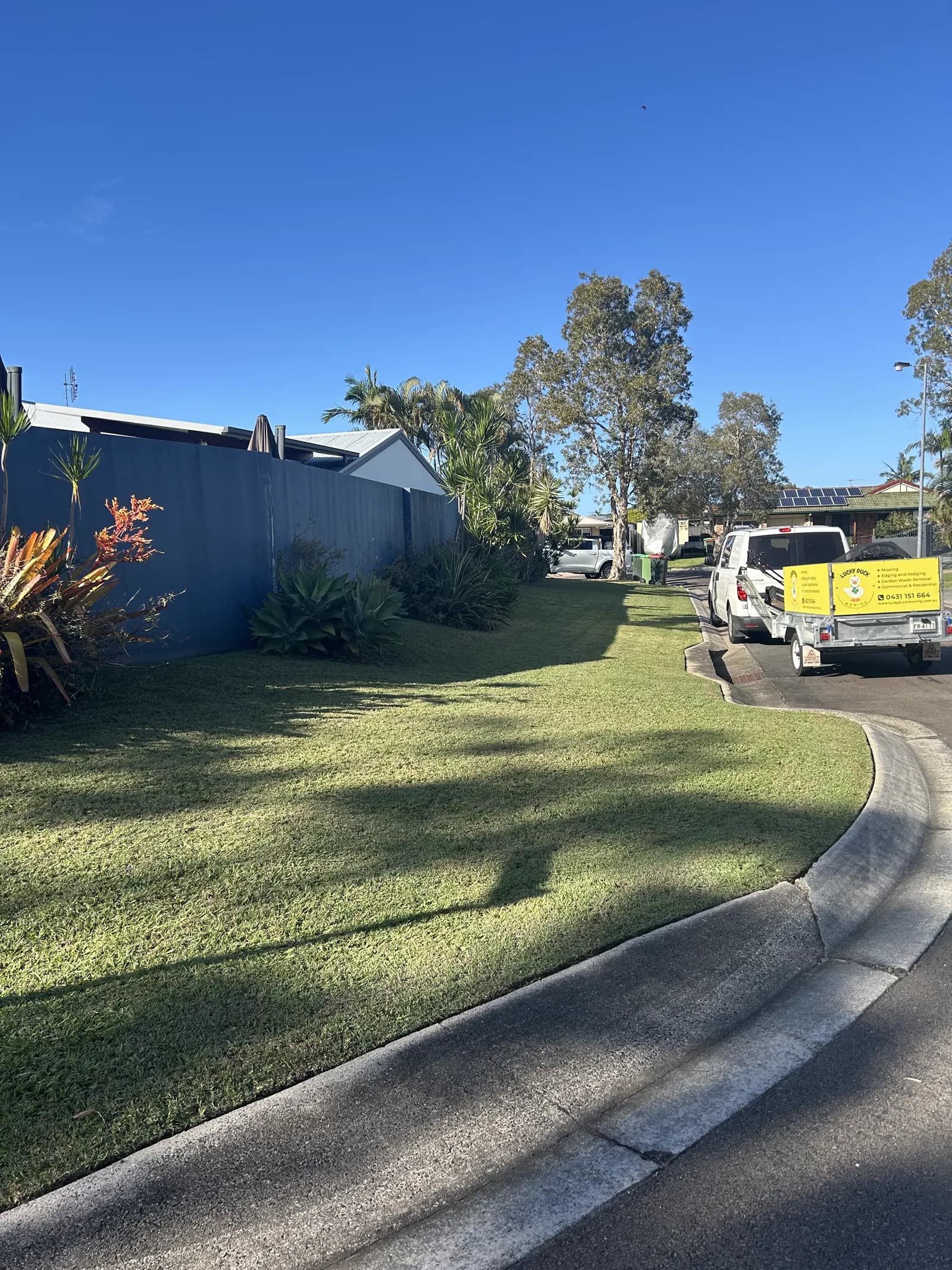 Lucky Duck Mowing branded trailer and ute parked on a finished lawn in Caloundra